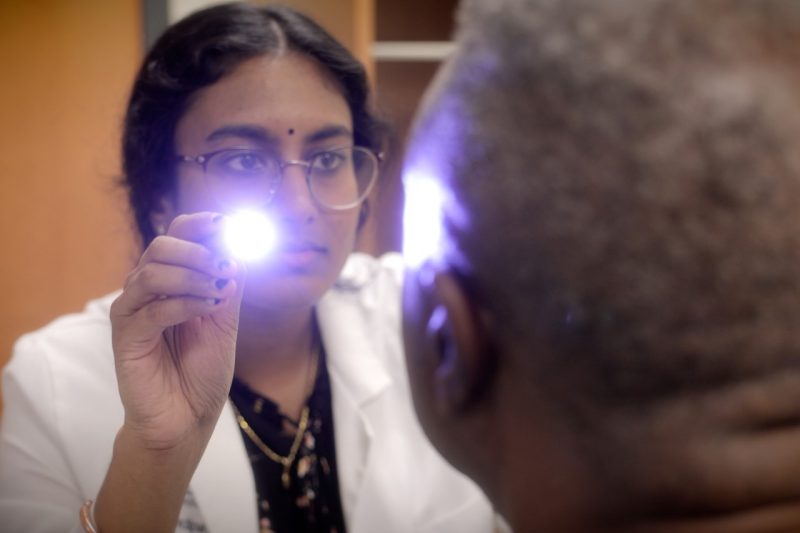 Medical student shines light into volunteer patieent's eyes.