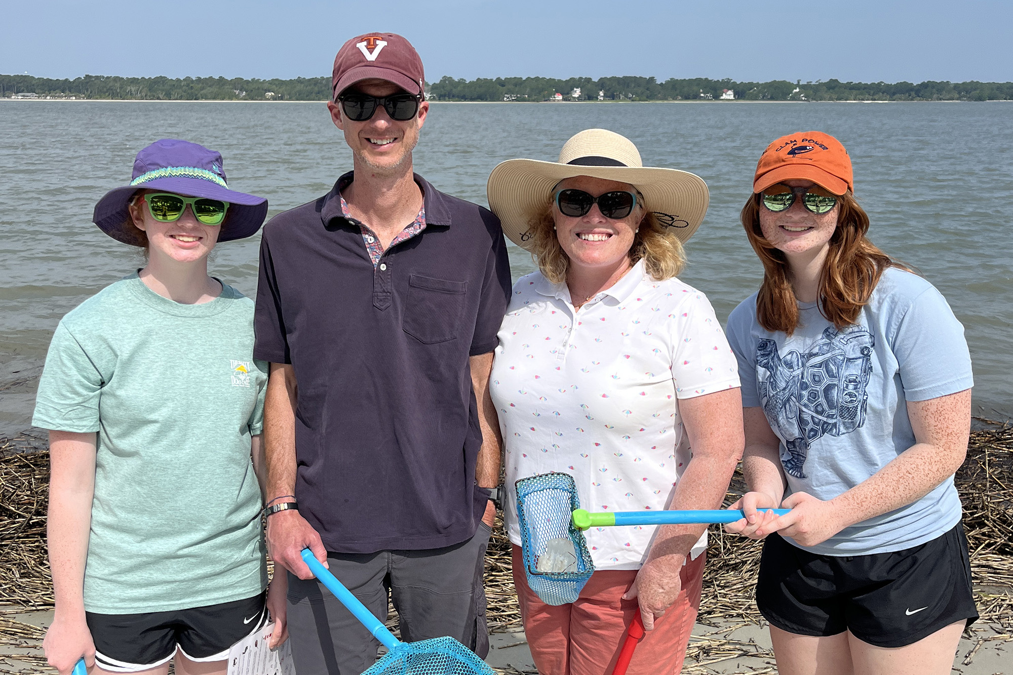 Family standing on a beach with hats, sunglasses, and crabbing gear.
