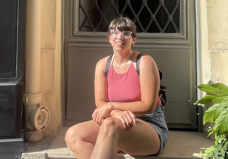 Person sitting on the steps of an old building in the summertime.