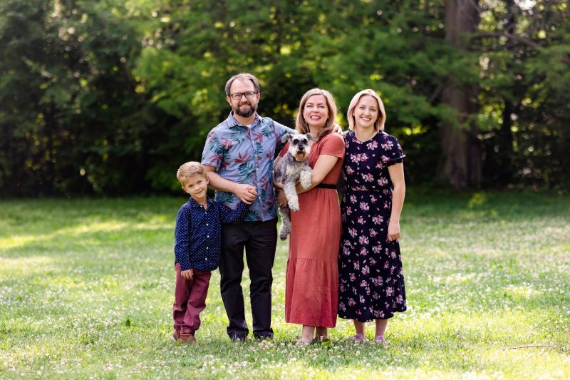 Family standing in a grassy field with trees behind them.