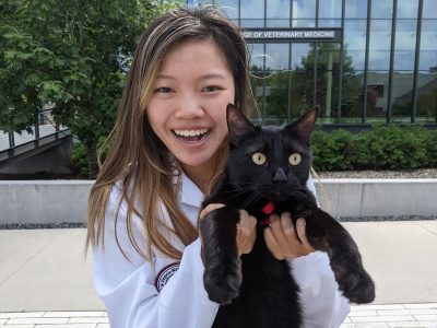 Person smiling and holding a black cat.