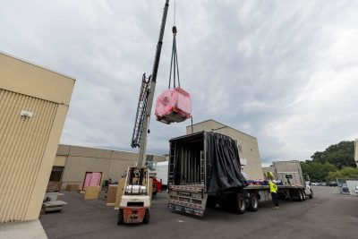 A crane unloads part of a MRI machine from the back of a flatbed truck.