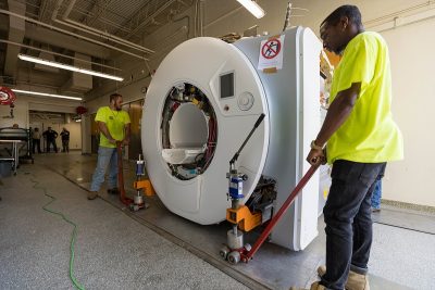 Two workers moving part of a new MRI machine down a hallway.