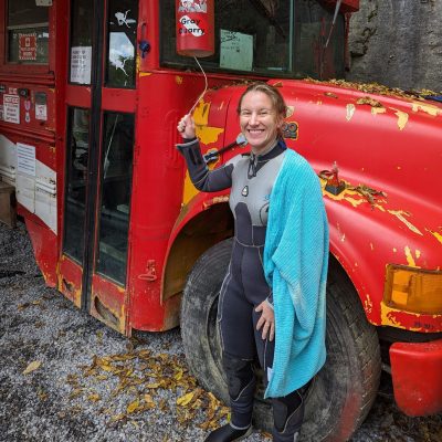 Person in scuba gear standing in front of a red bus.