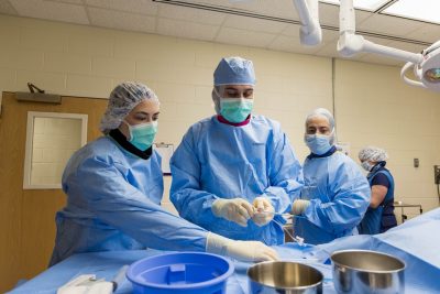 Audrey Keebaugh, Giulio Menciotti, and Justin Ganjei in blue surgical gowns preparing for surgery.