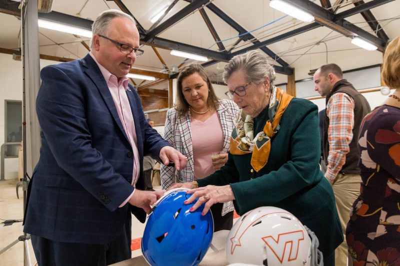 A faculty showing sports helmets to supporters.