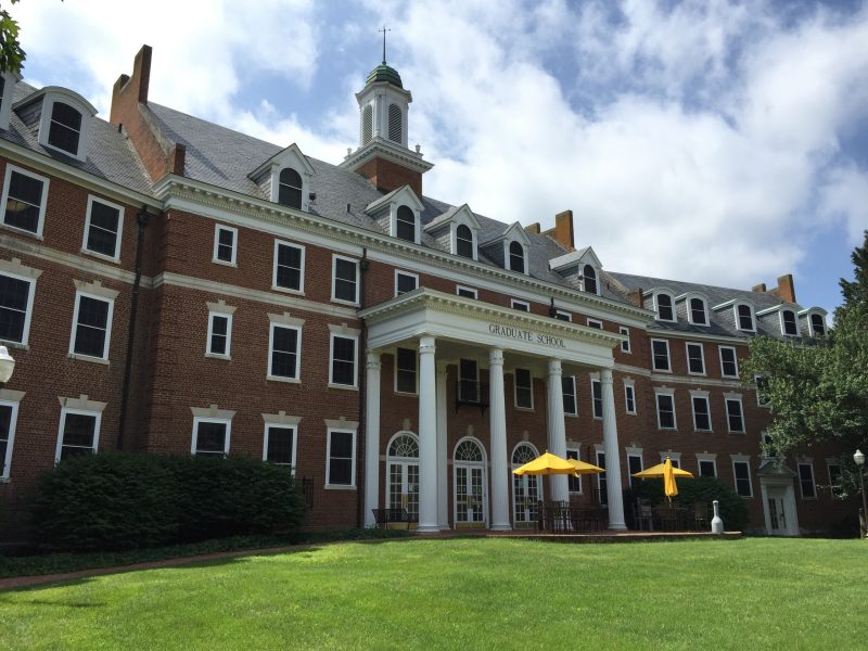 The Alumni Hall side of the Graduate Life Center in summer with the yellow umbrellas open over the tables on the patio