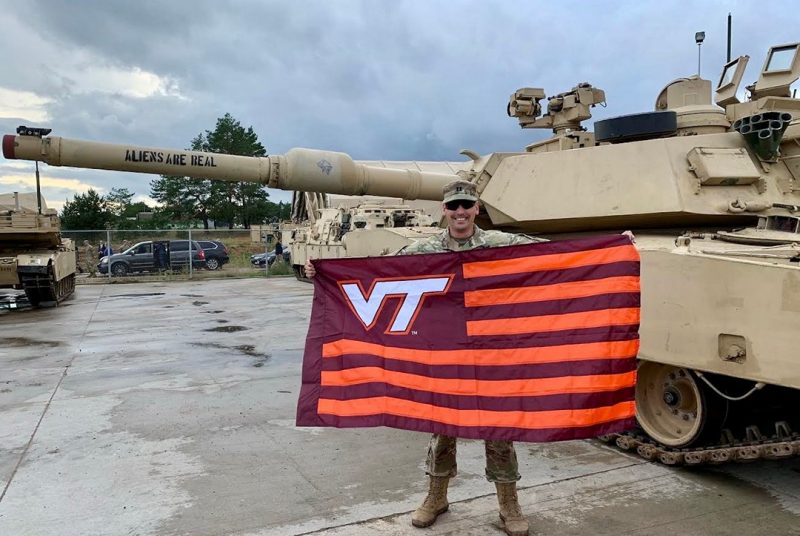 U.S. Army Capt. Daniel Gaines holds a Virginia Tech flag in front of a tank.