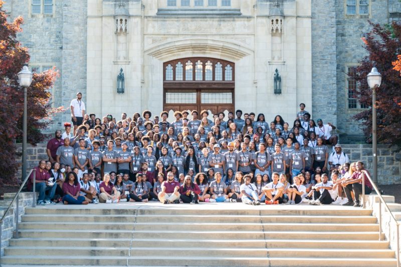 All attendees from the Black College Institue summer session e are gathered on the steps in front of the hokie stone backdrop of Burruss Hall. It is about 150 students. They are all dressed in grey tshirts. Staff and faculty are wearing chicago maroon. 