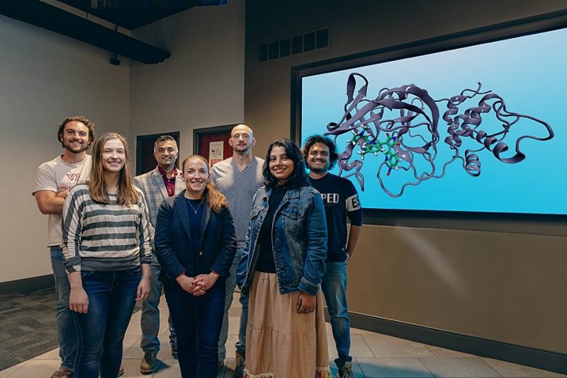 faculty member and students stand in a group in front of screen with molecule shown
