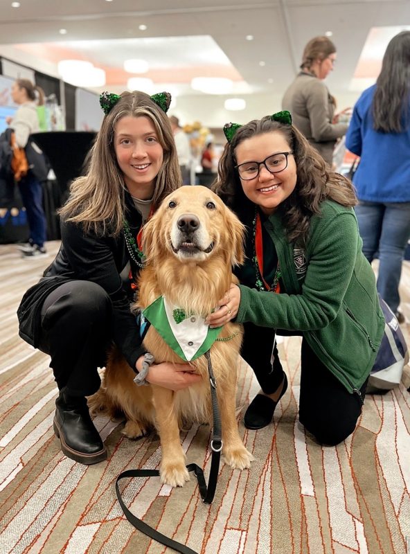 Two students with a dog at a conference.